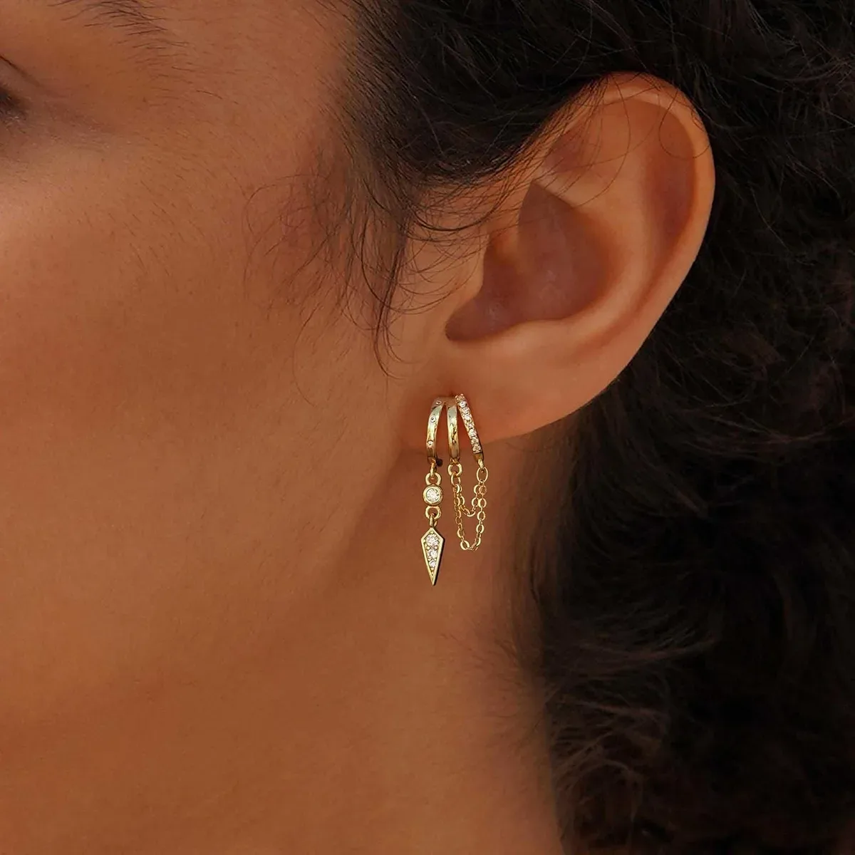 Side angle of gold dangle huggie earrings with the chain hanging