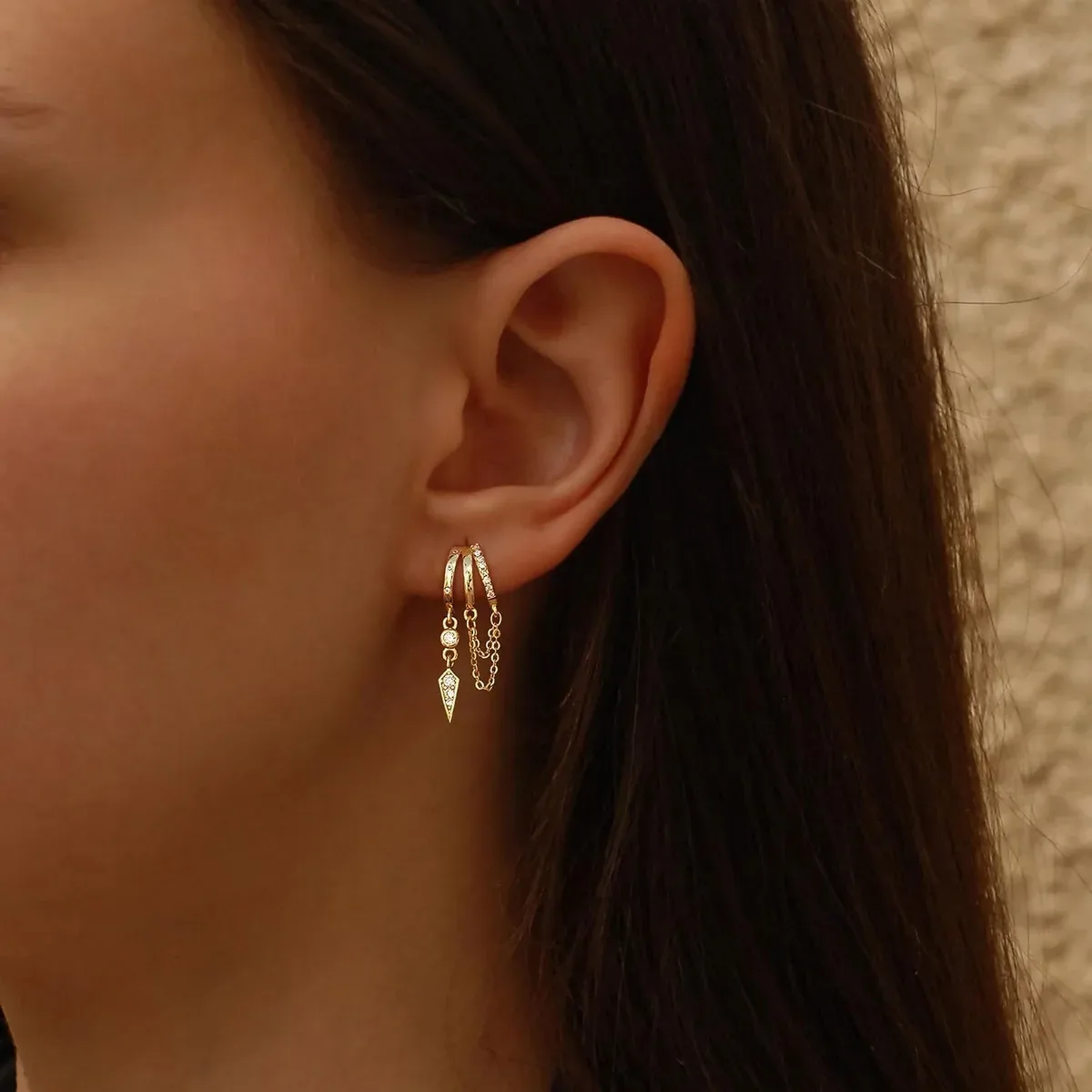 Gold dangle huggie earrings creating a stacked look on a model